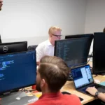 a group of men sitting at a table working on computers