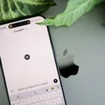 A smartphone shows a ChatGPT interface placed on an Apple laptop in a leafy environment.