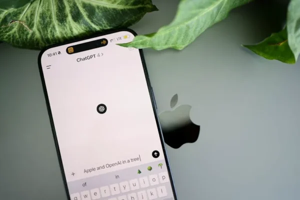 A smartphone shows a ChatGPT interface placed on an Apple laptop in a leafy environment.