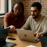 A software development team collaborating around a table with laptops and digital devices in a modern office setting