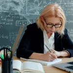 A woman writing in a notebook at a desk.