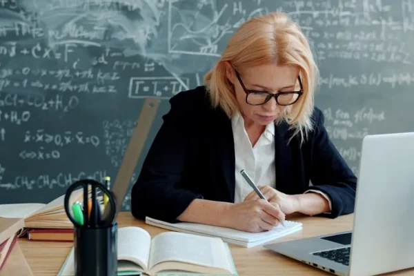 A woman writing in a notebook at a desk.