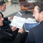 Three businessmen discussing financial documents in a modern office setting.