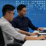 two men sitting at a table with laptops
