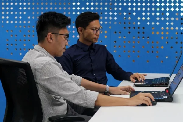 two men sitting at a table with laptops
