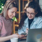 Two women collaborate on a laptop.